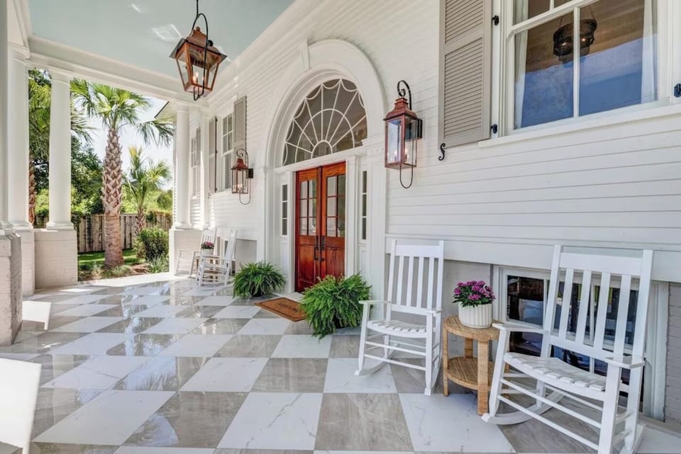 Front porch with a marble checkerboard floor, white rocking chairs and the arched front door